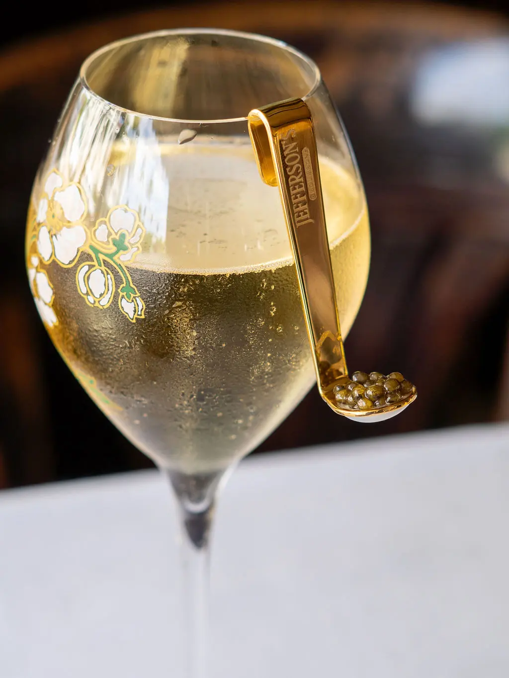 A glass of champagne with a gold spoon of caviar on its rim
